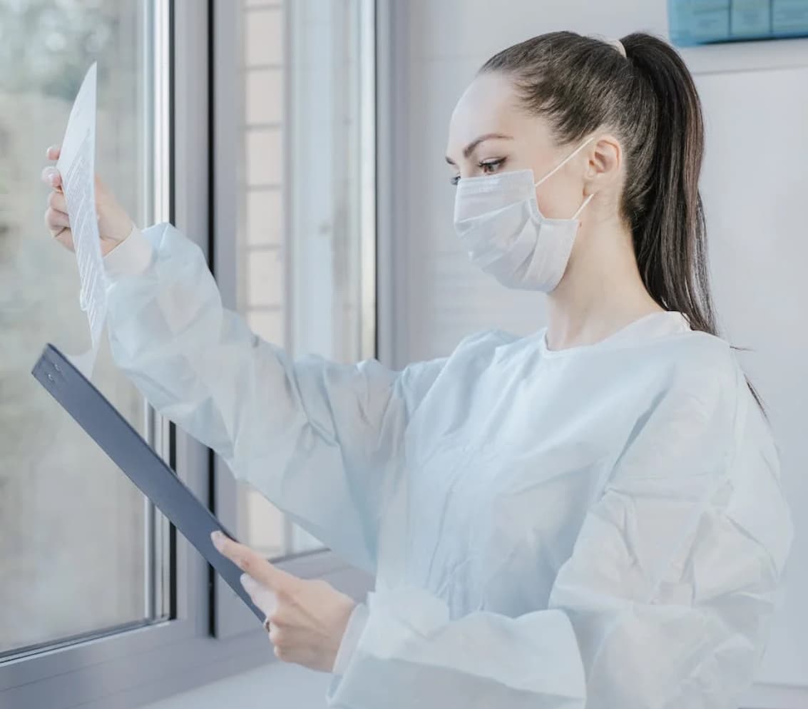 A healthcare worker in a mask and protective gown examining paper